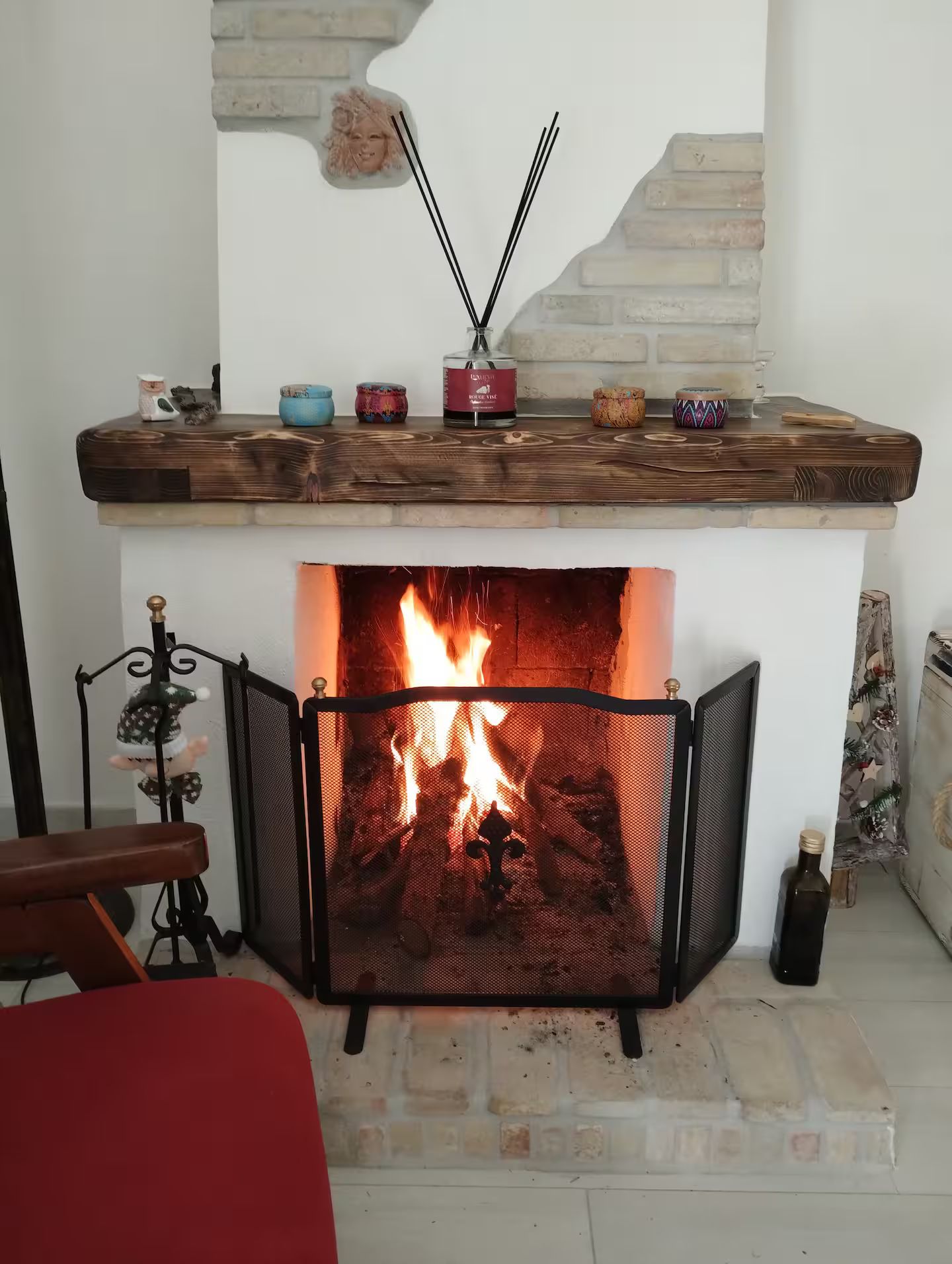 Une cheminée avec un feu, une étagère ornée d’objets décoratifs et un coin salon avec un fauteuil.
