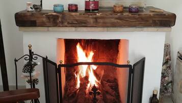 Une cheminée avec un feu, une étagère ornée d’objets décoratifs et un coin salon avec un fauteuil.