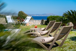 A terrace with lounge chairs, a table with a glass of drink, and a view of the sea. - Villa Aqua in Lachania (Lachania)