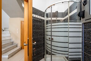 Ein modernes Badezimmer mit einer Duschkabine aus Glas, einer Holztür und einem gefliesten Boden.