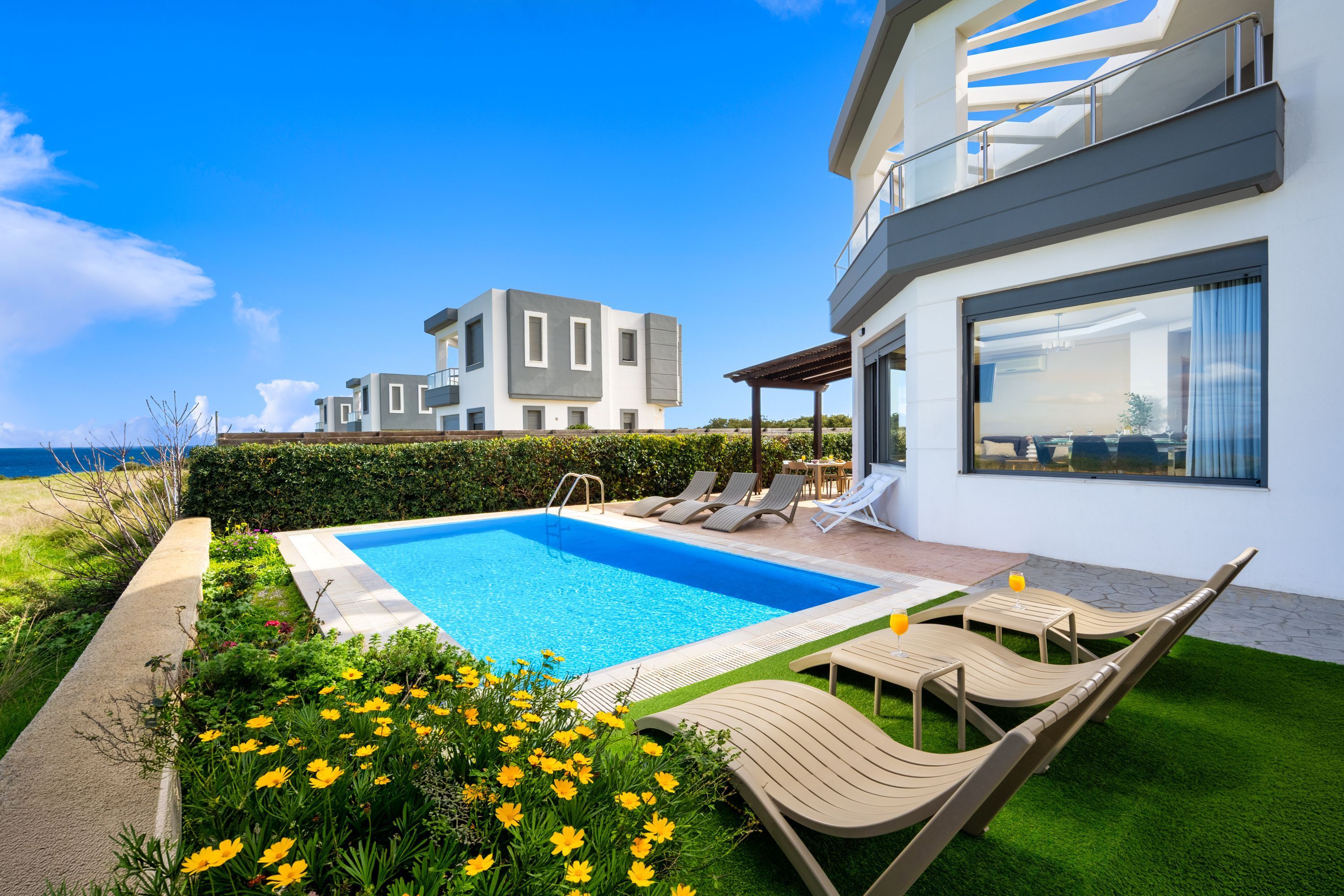 Ein moderner Poolbereich mit klarem, blauem Pool, Liegestühlen und Blick auf das Meer.