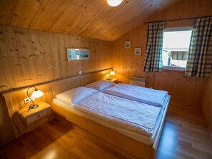 A wooden room with a bed, two bedside lamps, a window with curtains, and a wall-mounted picture. - Cabin in Annaberg With Swimming Pool (Annaberg-Lungoetz)