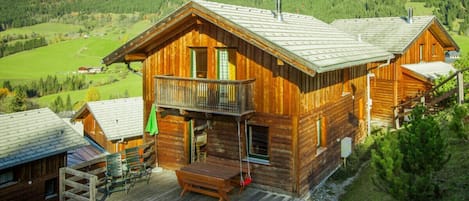 Una cabaña de madera con balcón, terraza y vistas a un paisaje montañoso.