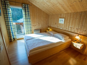 A wooden-paneled bedroom with a bed, a nightstand, a lamp, and a view of a balcony. - Cabin in Annaberg With Swimming Pool (Annaberg-Lungoetz)