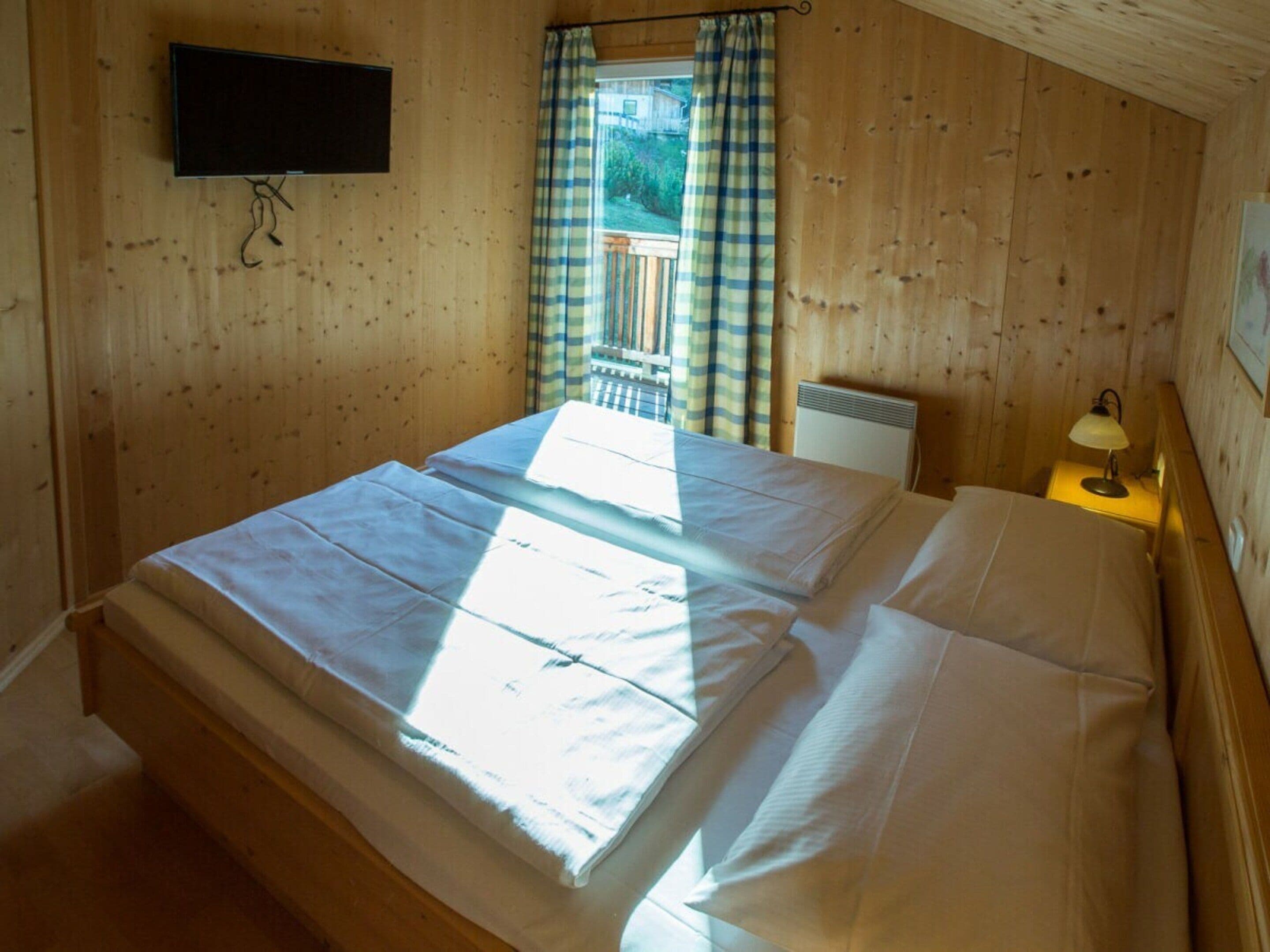 A room with a bed, a television mounted on the wall, and a window with curtains.
