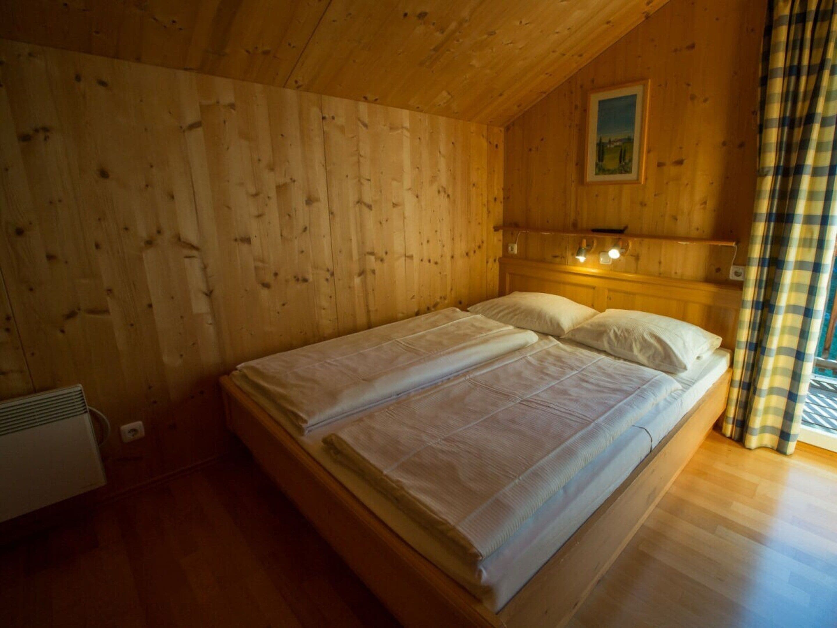 Une pièce de cabane en bois comprenant un lit, un tableau accroché au mur et une fenêtre avec des rideaux.