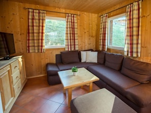 A wooden cabin interior with a sofa, a small table with a plant, and a television on a wooden cabinet. - Cabin in Annaberg With Swimming Pool (Annaberg-Lungoetz)