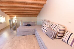 A modern loft bedroom with a wooden ceiling, a glass railing, a sofa, and striped pillows. - Mon Emvasia Margarites Villa A (Rethymno)