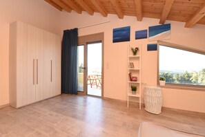 A room with a wooden floor, a sliding glass door leading to an outdoor area, a white wardrobe, and a window with a view. - Mon Emvasia Margarites Villa A (Rethymno)
