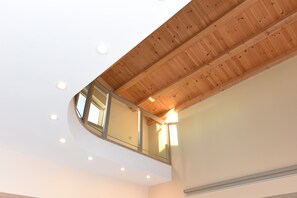 A high ceiling with wooden beams, recessed lighting, and a glass railing overlooking a lower level. - Mon Emvasia Margarites Villa A (Rethymno)