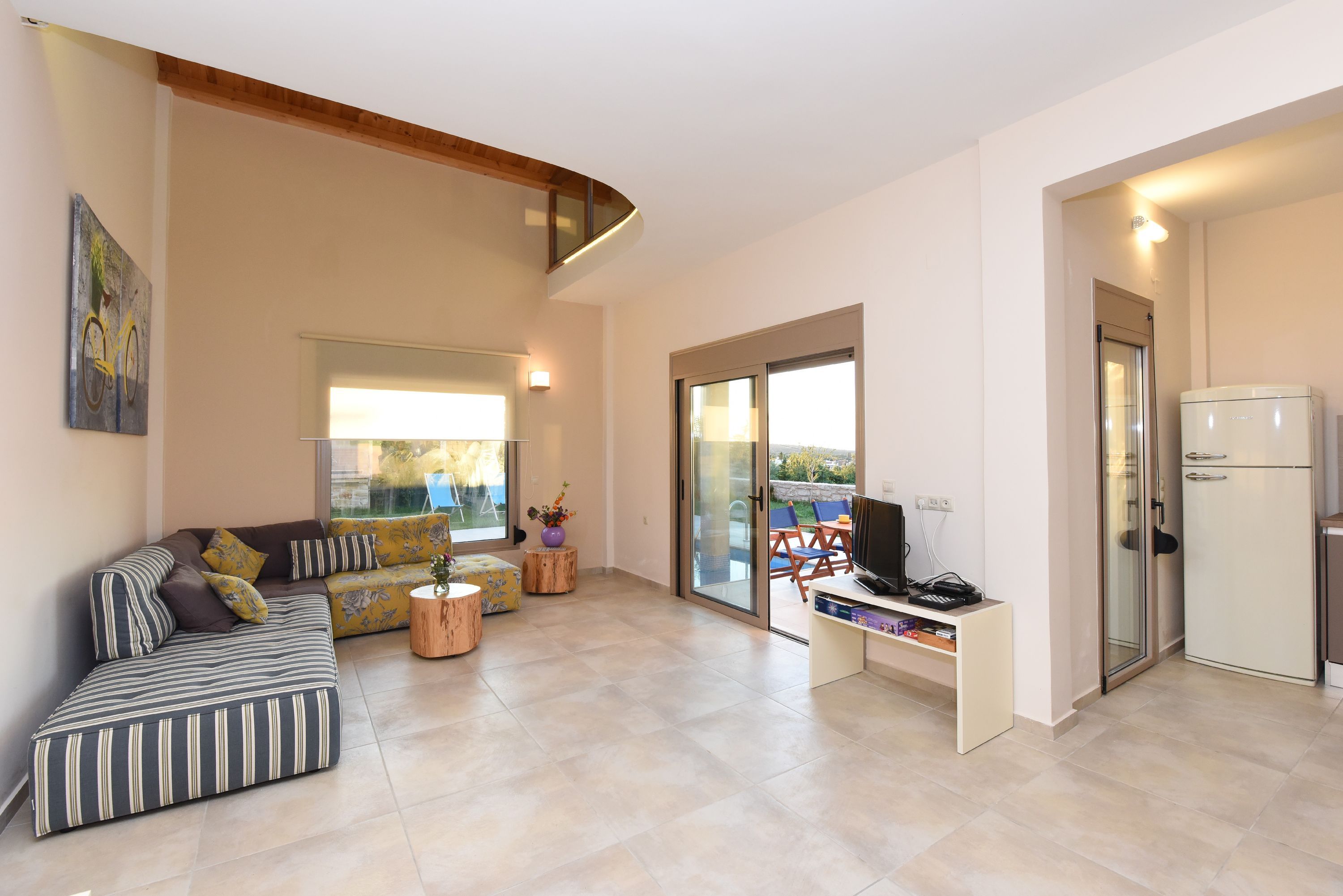 A modern living room with a sofa, a television, and a kitchen area with a refrigerator.