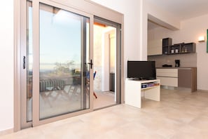 Ein moderner Wohnraum mit einer Schiebeglastür, die auf einen Balkon führt, einem Flachbildfernseher auf einem Schrank und einer Küchenzeile.