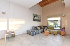 Un salon moderne avec un canapé d’angle, une petite table d’appoint et une grande fenêtre donnant sur l’extérieur.