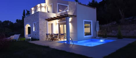 A modern house with a swimming pool, outdoor seating, and a stone facade.