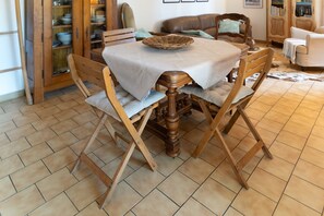 A dining area with a wooden table and chairs, a woven basket on the table, and a tiled floor.