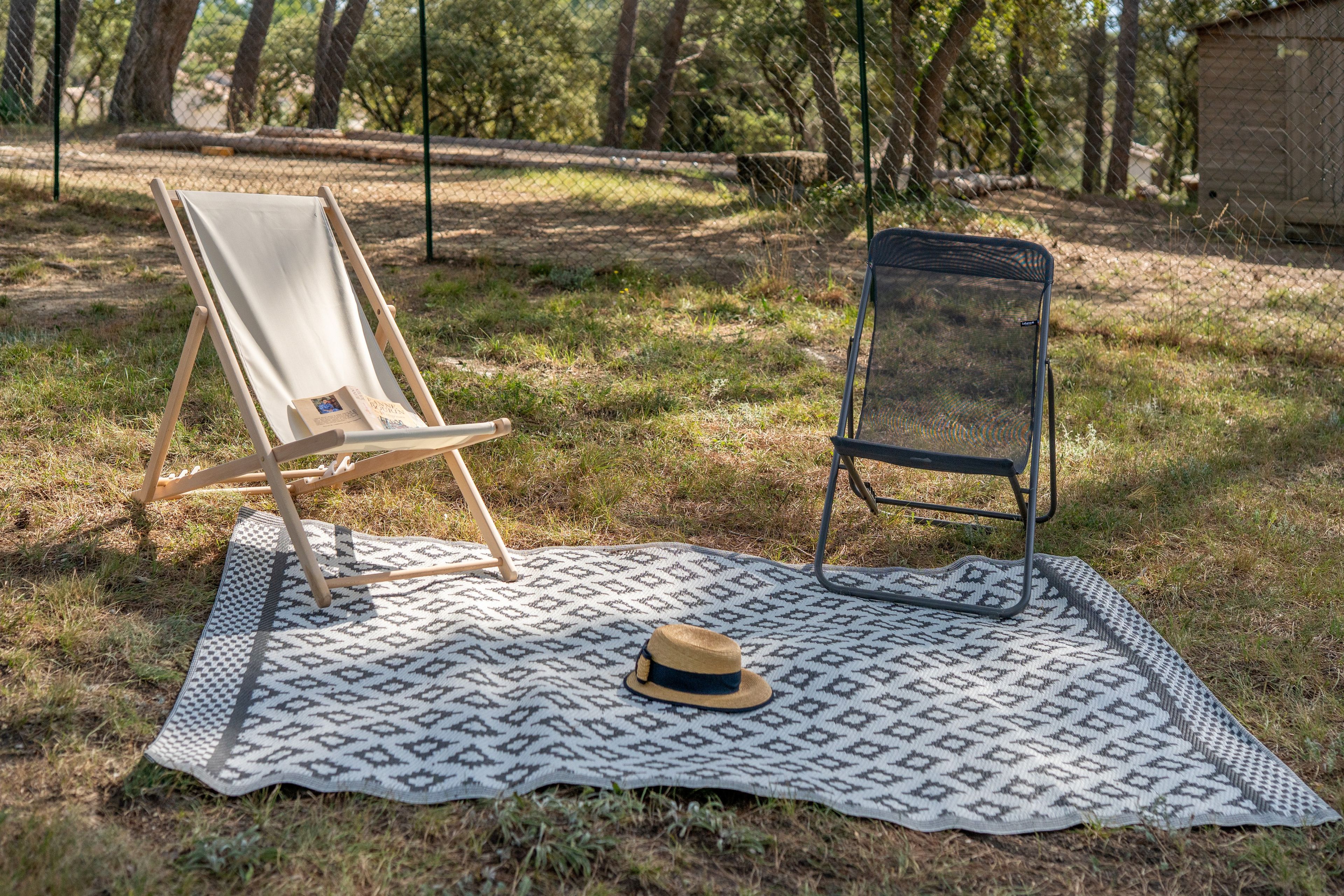 A picnic setup with a blanket, two chairs, and a hat on the grass.