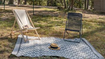 A picnic setup with a blanket, two chairs, and a hat on the grass.