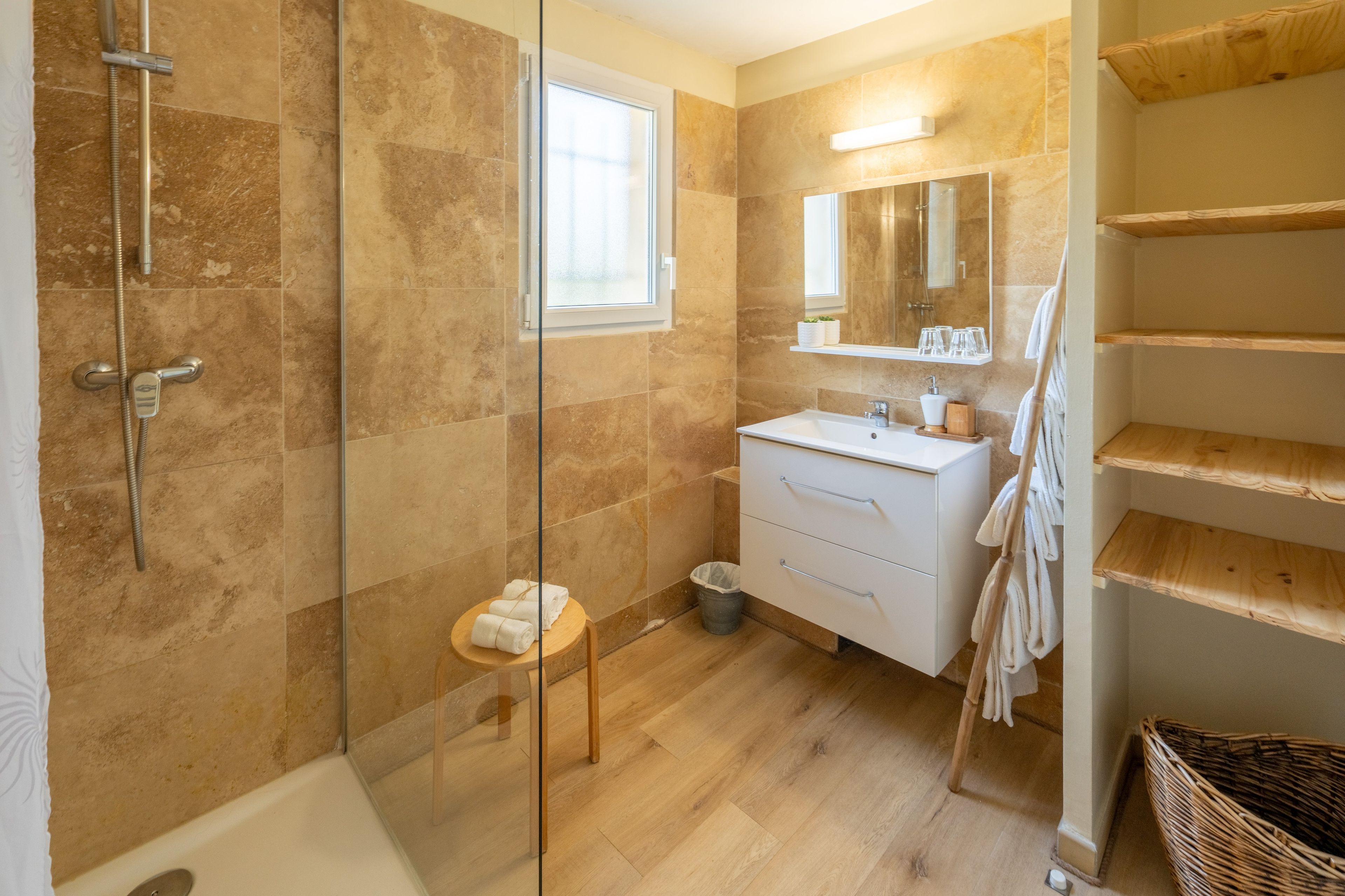 Une salle de bain moderne avec une douche à parois de verre, un lavabo avec un miroir au-dessus et des étagères en bois.