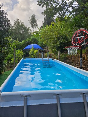 Une piscine extérieure avec un panier de basketball et un parasol bleu.