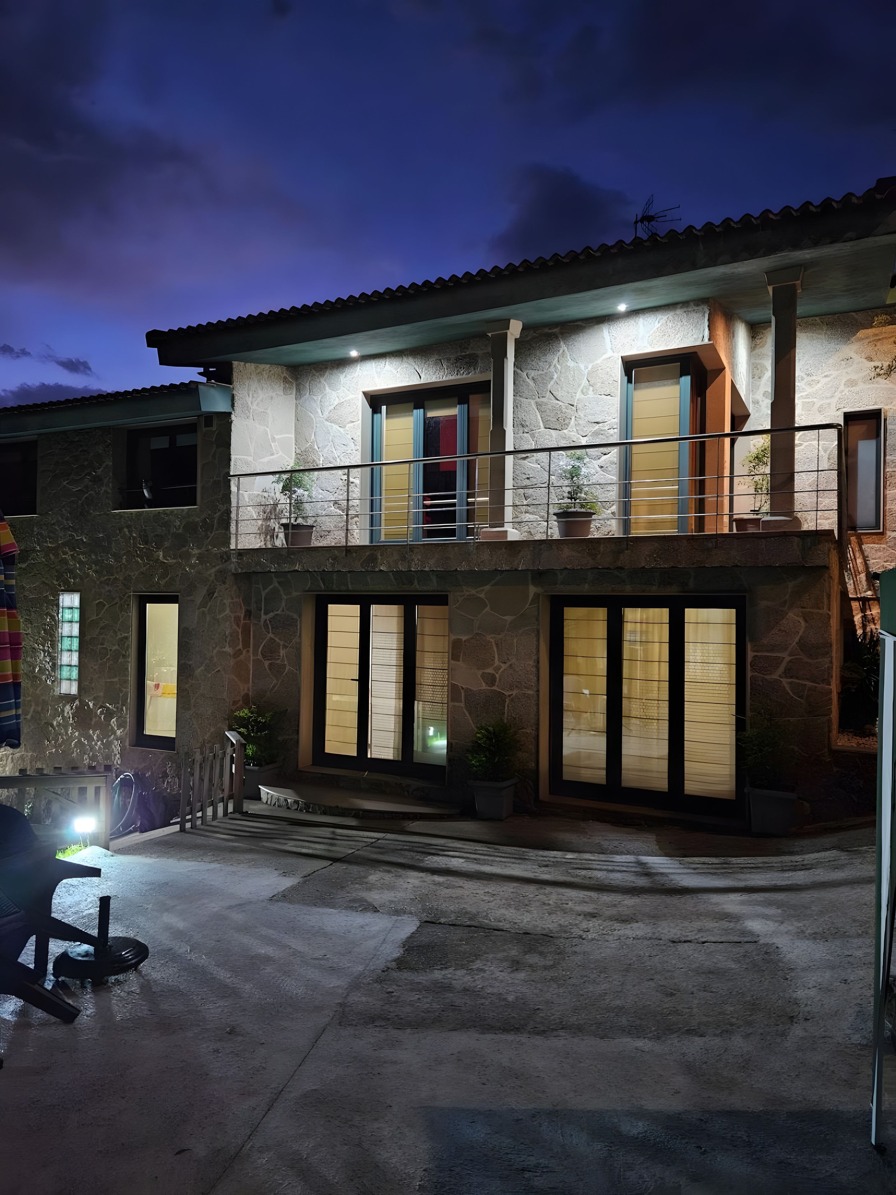 Una casa de dos pisos con fachada de piedra, múltiples ventanas y un balcón con barandilla.