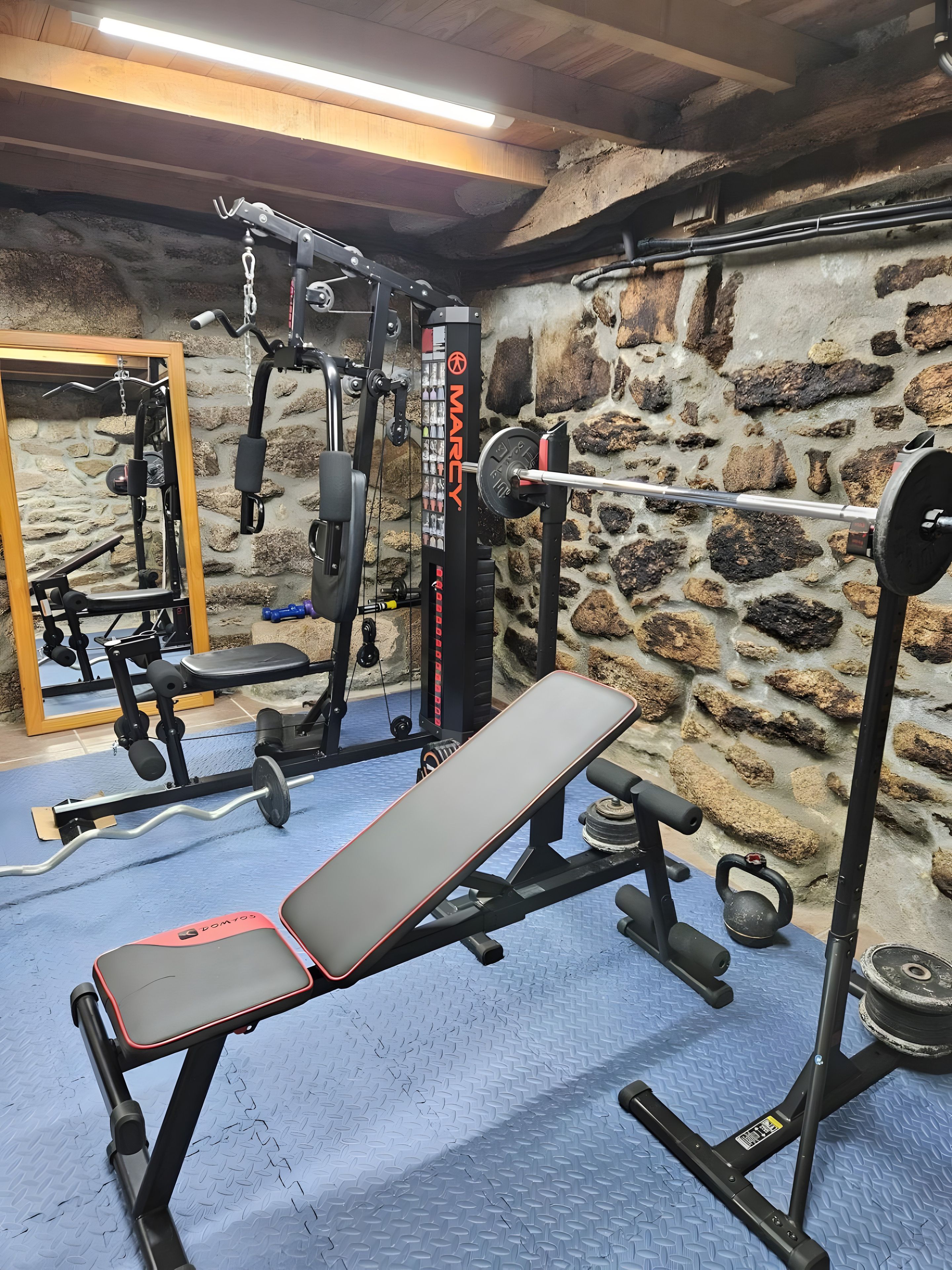 A gym with a stone wall, a bench, and various exercise equipment.