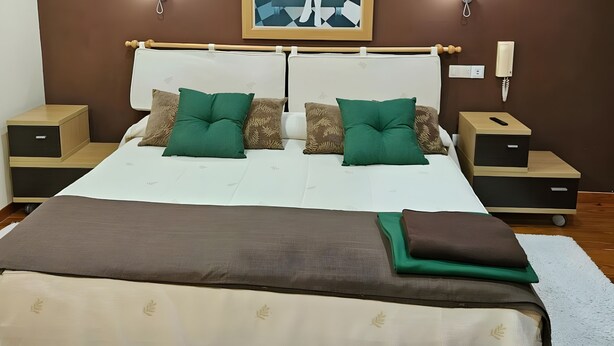 A bedroom with a large bed, two bedside tables, a wall-mounted light, and a painting.