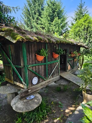 A rustic wooden structure with a moss-covered roof, green accents, and potted plants.