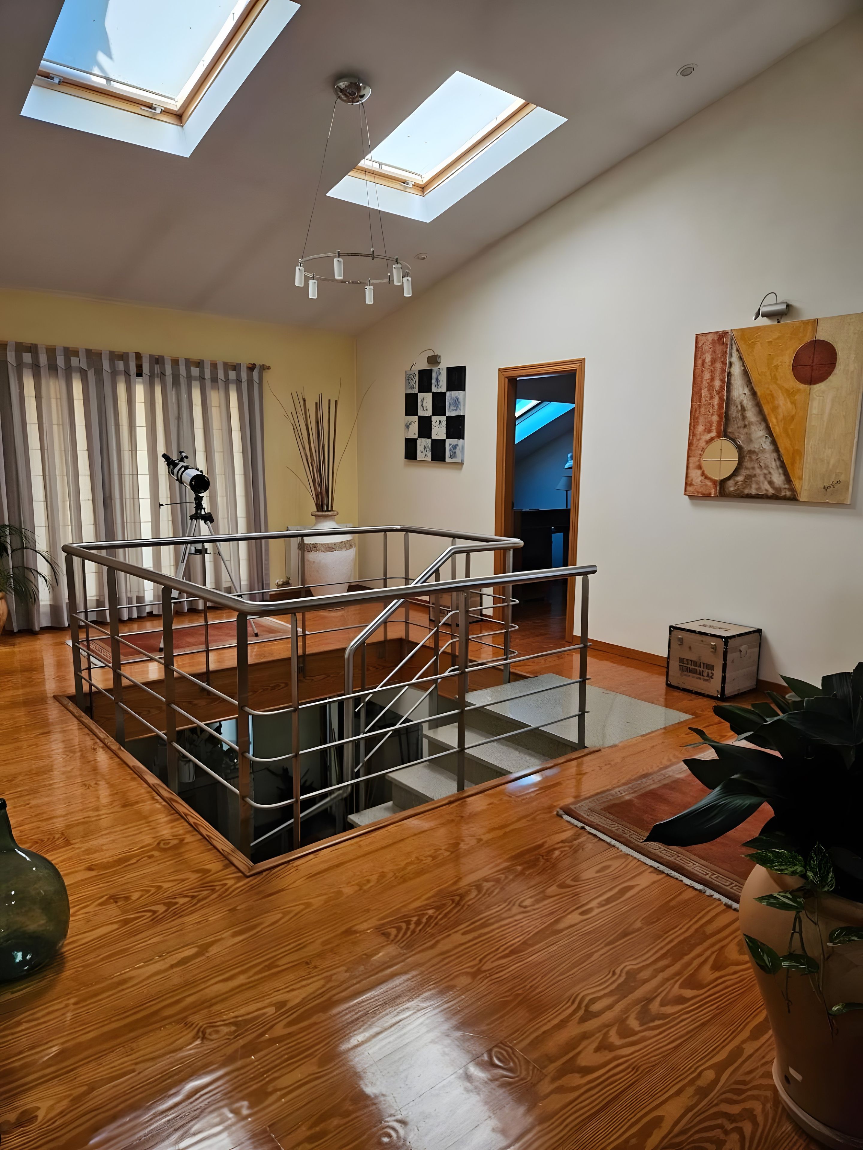 Un amplio salón con suelo de madera, una escalera de cristal y un tragaluz.