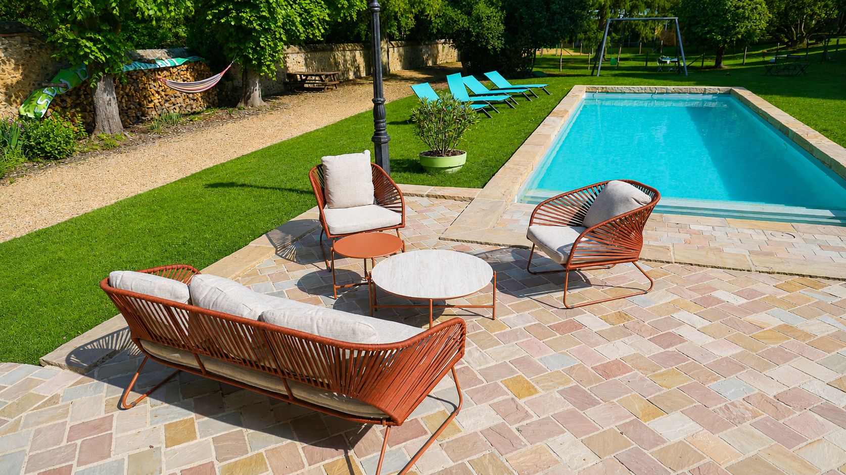 Un espace aménagé au bord de la piscine, avec des meubles en osier, une terrasse en pierre et une pelouse bien entretenue.