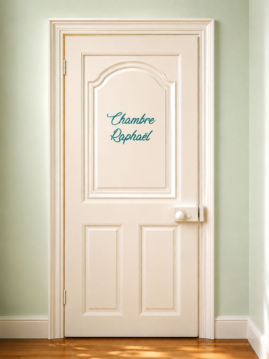 Une porte blanche sur laquelle est inscrit en lettres cursives le nom « Chambre Raphaël ».