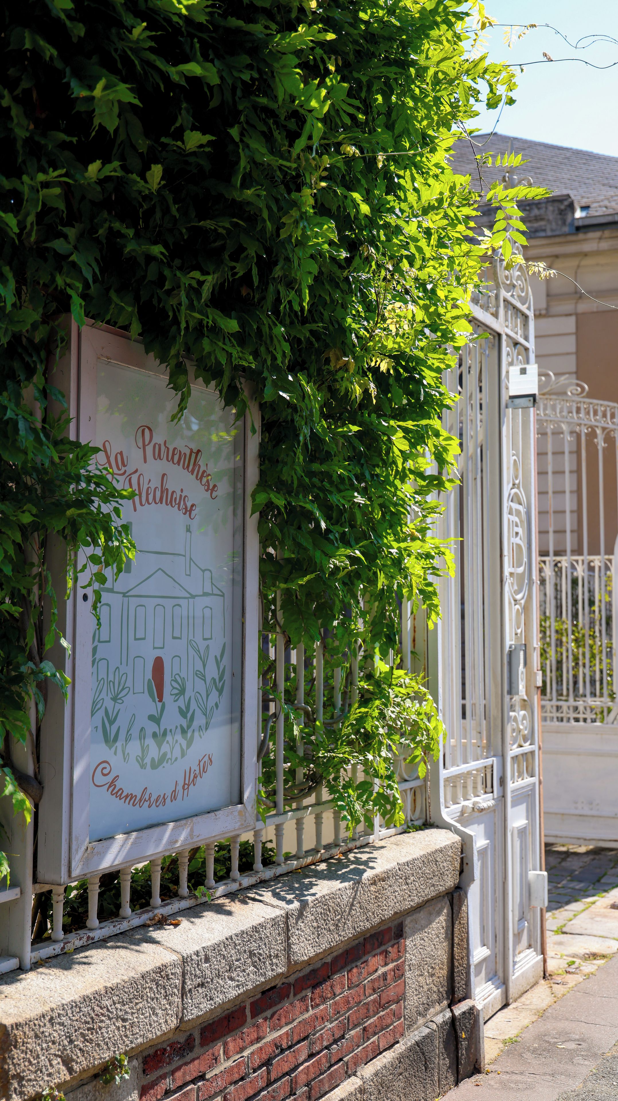 Une enseigne illustrant un bâtiment et comportant du texte, une porte en métal blanche et un mur de briques.
