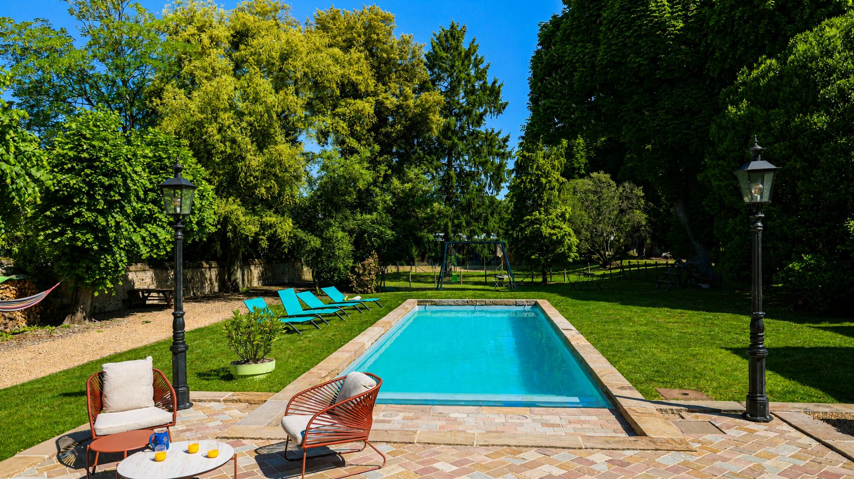 A rectangular swimming pool with a tiled border, surrounded by a well-maintained lawn and trees.