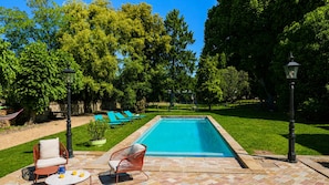 A rectangular swimming pool with a tiled border, surrounded by a well-maintained lawn and trees.