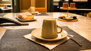 A dining table with a cup of coffee, a pastry, and condiments.