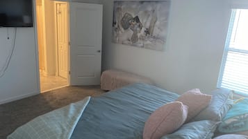 A bedroom with a bed, a painting, a television, and a door.