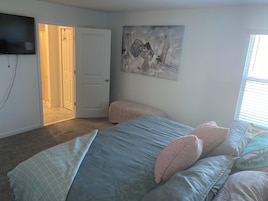 A bedroom with a bed, a painting, a television, and a door.