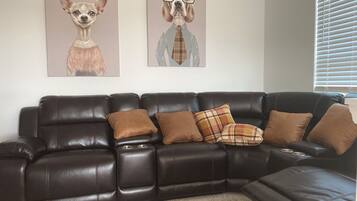 A dark brown leather sectional sofa with multiple cushions, a carpeted floor, and two wall-mounted dog portraits.
