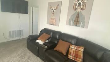 A living room with a black leather sofa, two brown pillows, a plaid pillow, and a black coffee table with two metallic bowls.