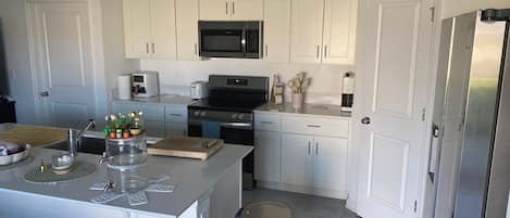 A modern kitchen with white cabinetry, stainless steel appliances, and a central island with a sink and countertop.