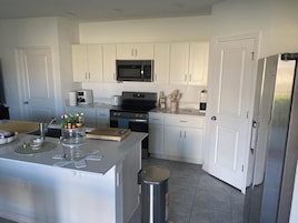 A modern kitchen with white cabinetry, stainless steel appliances, and a central island with a sink and countertop.