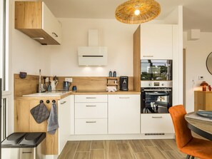 A modern kitchen with a built-in oven, a coffee machine, and a dining area with a table and orange chair. - Central apartment with parking - 4 guests (Saint-Michel-Chef-Chef)