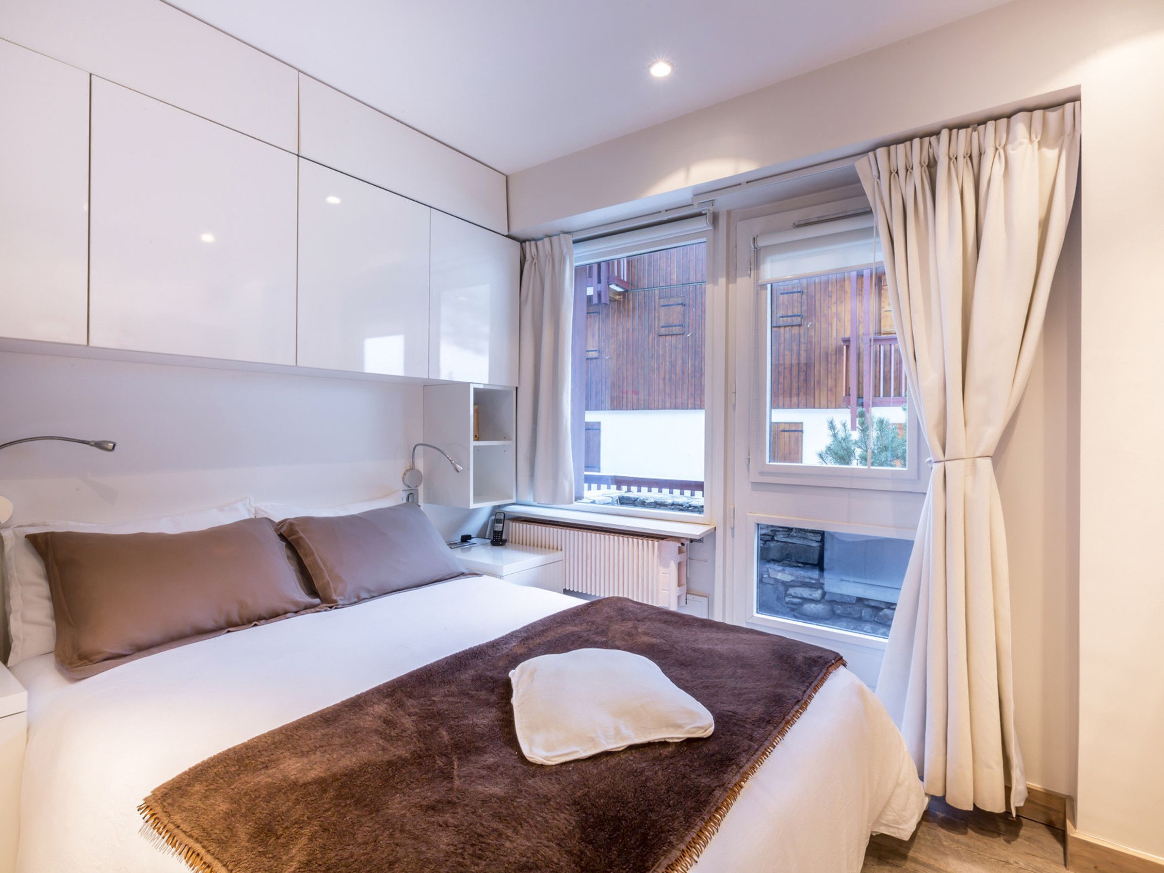Un dormitorio con cama, mesita de noche, ventana con cortinas y vistas al exterior.
