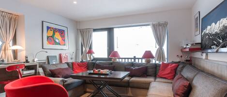 A modern living room with a sofa, red chair, and a dining table.