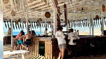 Un bar en la playa con terraza de madera y techo de paja.
