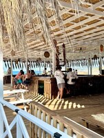 Un bar en la playa con terraza de madera y techo de paja.