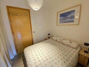 Ein Schlafzimmer mit Holztür, einem Bett mit gemustertem Überwurf, einem Nachttisch mit Lampe und einem gerahmten Bild an der Wand.