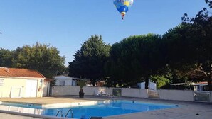 A clear blue sky with a hot air balloon in the distance, a swimming pool, and surrounding trees.