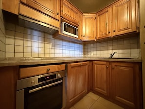 Eine Küche mit Holzschränken, einer Mikrowelle, einem Backofen und einer gefliesten Spritzschutzwand.