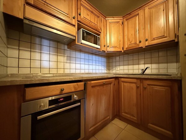 Una cocina con armarios de madera, microondas, horno y salpicadero de azulejos.
