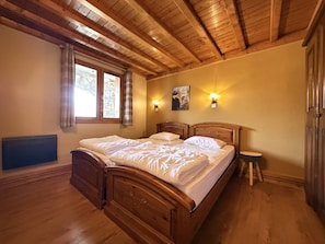A bedroom with a wooden ceiling, a bed with white bedding, a small stool, and a wall-mounted light fixture. - Ski-in/ski-out apartment - 6 guests (Belle Plagne)